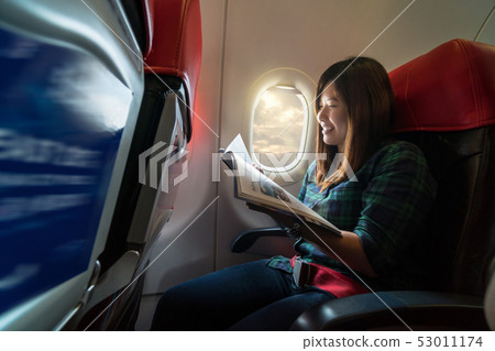 Asia young woman reading the magazine while traveling inside the airplane beside the window, traveler and transportation concept Asia young woman reading the magazine while traveling inside the airplane beside the window, traveler and transportation concept 53011174