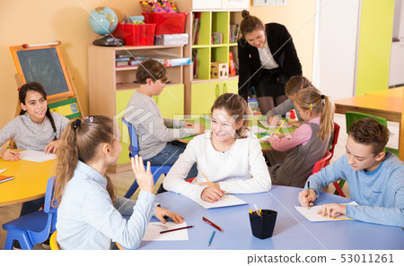 boys and girls sitting and teacher helping drawing boys and girls sitting and teacher helping drawing 53011261