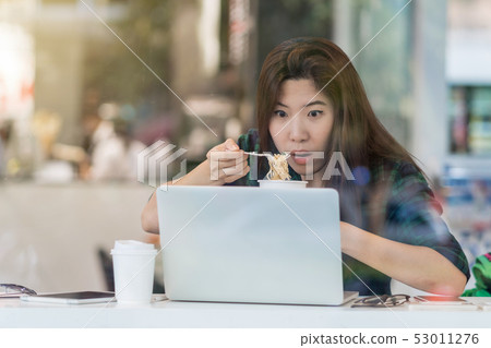 Portrait of asian businesswoman in casual suit eating noodles with Shocked action in rush hour at the desk beside the glass in modern office, Business work hard concept 53011276