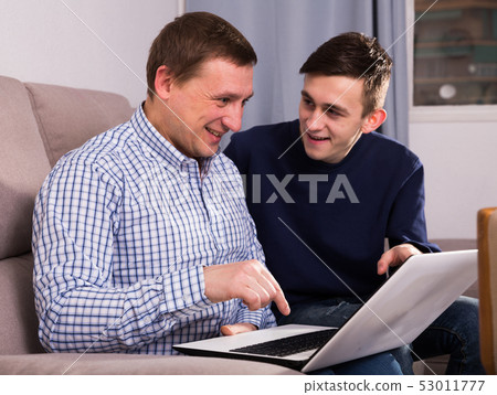 Adult male with his son are resting together and playing on laptop Adult male with his son are resting together and playing on laptop 53011777