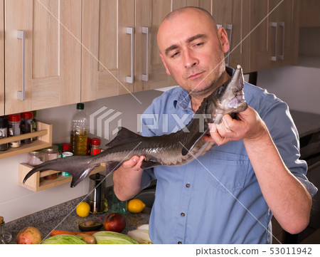 Smiling man standing holding uncooked sturgeon Smiling man standing holding uncooked sturgeon 53011942