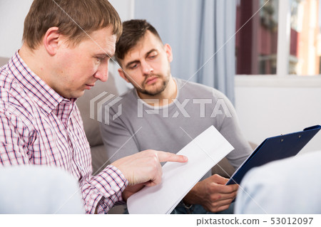 Troubled man discussing documents with partner on couch 53012097