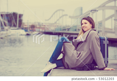 woman with luggage posing at quay and smiling 53012203