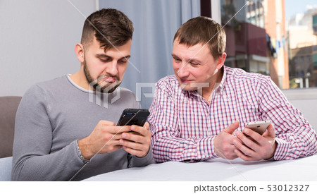 Men with phone discussing at home 53012327
