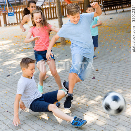 Happy children playfully running after ball outdoors in park Happy children playfully running after ball outdoors in park 53012334