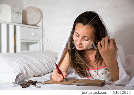 Adult woman writing in diary and laying in bed at night 53012633