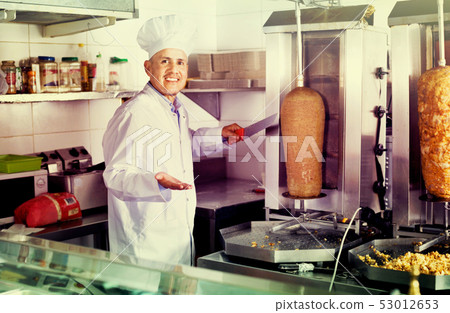 Cheerful mature man cook cutting kebab meat on kitchen Cheerful mature man cook cutting kebab meat on kitchen 53012653