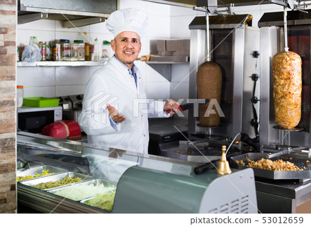 man chef wearing uniform cutting meat for kebab on kitchen in fast food restaurant man chef wearing uniform cutting meat for kebab on kitchen in fast food restaurant 53012659