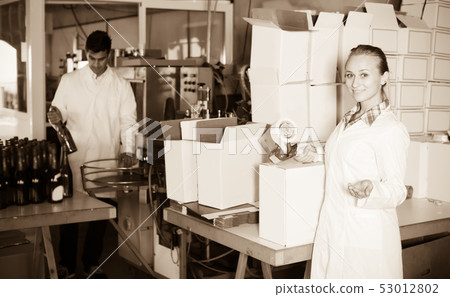 Happy woman in uniform packing wine bottles 53012802