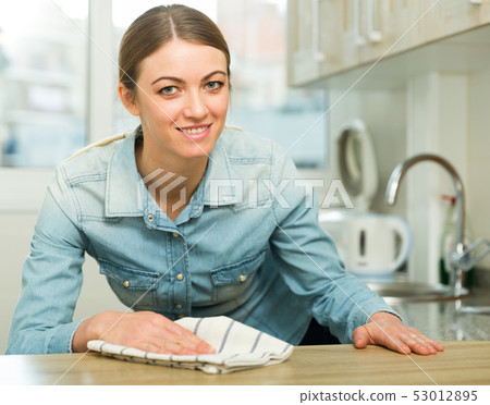 Positive housewife cleans the table in the kitchen 53012895