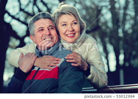 cheerful mature married couple sitting on park bench 53012994