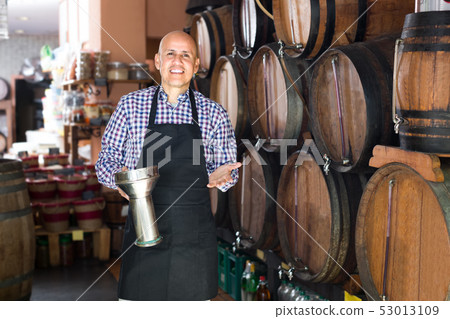 Satisfied mature man seller pouring wine from wood Satisfied mature man seller pouring wine from wood 53013109