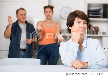 Upset mother is sitting at the table and her family is sympathying with her 53013759