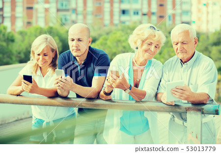 Portrait of positive mature couples using gadgets in park 53013779