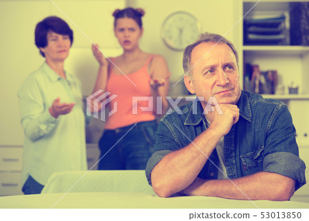 Woman and her daughter are sympathying their sad father who is sitting at the table Woman and her daughter are sympathying their sad father who is sitting at the table 53013850