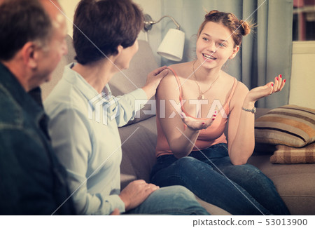 Marrieds with their adult daughter are talking together on sofa 53013900