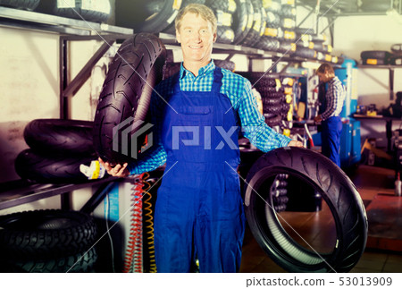 Mature professional mechanic holding new tyre for motorcycle Mature professional mechanic holding new tyre for motorcycle 53013909