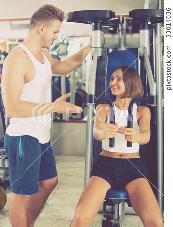 Man coach assisting woman in using pec deck Man coach assisting woman in using pec deck 53014036