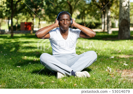 Athletic african american in headphones sitting before training in park 53014079