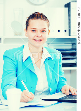 Young office worker is working with documents and laptop 53014090