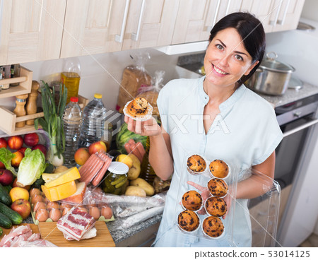 Cheerful woman is posing with cupcakes in time cooking on the kitchen Cheerful woman is posing with cupcakes in time cooking on the kitchen 53014125