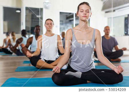 Sporty girl meditating in yoga position Padmasana during group training Sporty girl meditating in yoga position Padmasana during group training 53014209