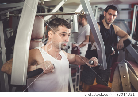 Guy training on fitness machine in gym Guy training on fitness machine in gym 53014331