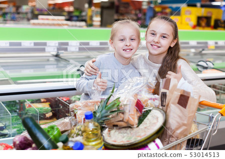 Two girls are standing with cart with products in the supermarket. Two girls are standing with cart with products in the supermarket. 53014513