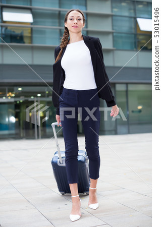 Female in suit with suitcase is staying near the building Female in suit with suitcase is staying near the building 53015496