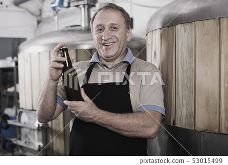 Adult brewer is standing with beer bottle Adult brewer is standing with beer bottle 53015499