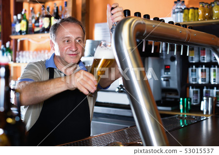 Barman is pouring unbottled beer with foam for client in the bar. Barman is pouring unbottled beer with foam for client in the bar. 53015537
