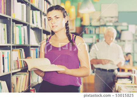 Teenage girl is choosing textbook for preparing to exam in bookstore. Teenage girl is choosing textbook for preparing to exam in bookstore. 53015825