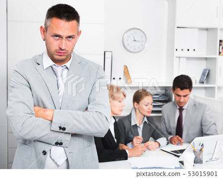 Unhappy man at office with working colleagues 53015901