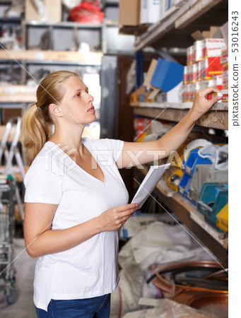Woman customer holding shop list and looking tools at shelves in store Woman customer holding shop list and looking tools at shelves in store 53016243