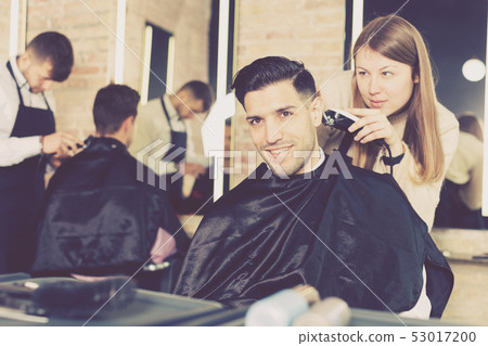 Woman barber making hairstyle for male with electric trimmer Woman barber making hairstyle for male with electric trimmer 53017200