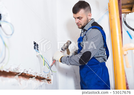 Male is beating a part of the wall with a hammer 53017676