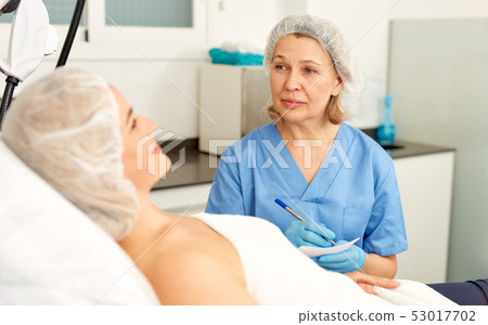 Skillful cosmetologist consulting young woman in medical esthetic office 53017702