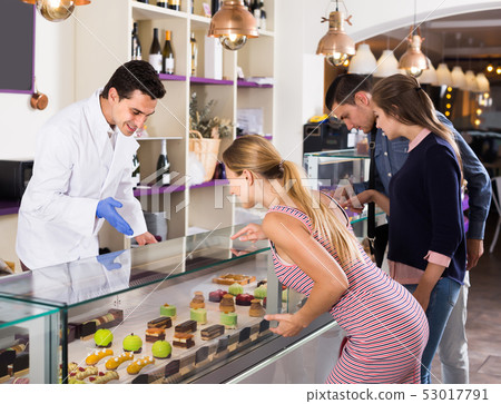 Laughing seller helping clients to choose sweets Laughing seller helping clients to choose sweets 53017791