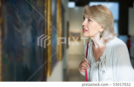 Mature woman standing in art museum near the painting in baguette Mature woman standing in art museum near the painting in baguette 53017832