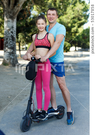 Father and preteen girl riding scooter Father and preteen girl riding scooter 53017858