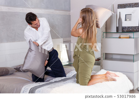 Loving couple fighting with pillows on bed Loving couple fighting with pillows on bed 53017986