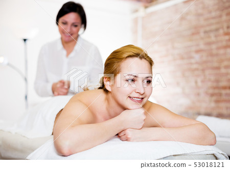 Masseuse massaging back zone of young smiling woman Masseuse massaging back zone of young smiling woman 53018121