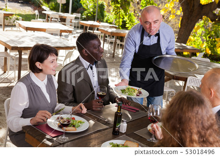 Waiter and four guests at open-air restaurant summer Waiter and four guests at open-air restaurant summer 53018496