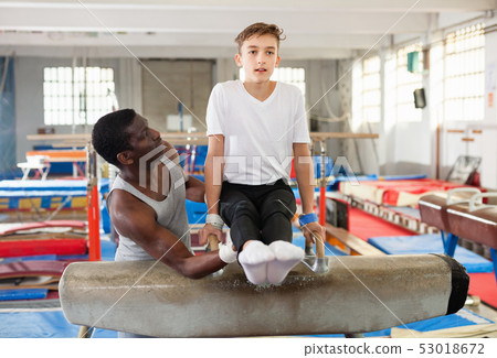 Male coach training teenage boy on gymnastic equipment at acrobatic hall Male coach training teenage boy on gymnastic equipment at acrobatic hall 53018672