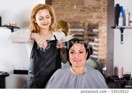 Hairdresser does to woman haircut with use of scissors and hairbrushes Hairdresser does to woman haircut with use of scissors and hairbrushes 53018822