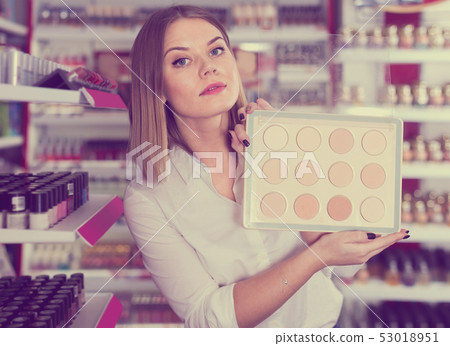 young female seller offering compact powder at store 53018951