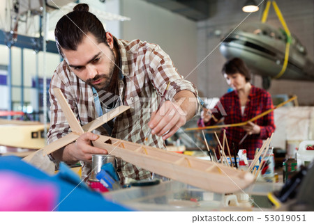 Young handsome bearded man enjoying his hobby - modeling light airplanes in aircraft hangar Young handsome bearded man enjoying his hobby - modeling light airplanes in aircraft hangar 53019051