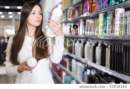 Serious young woman attentively looking hair shampoo Serious young woman attentively looking hair shampoo 53019163