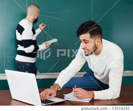 Students working with laptop near blackboard Students working with laptop near blackboard 53019295