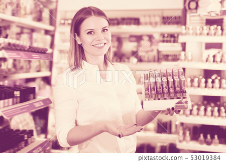 Positive salesgirl offering colors of lipstick Positive salesgirl offering colors of lipstick 53019384